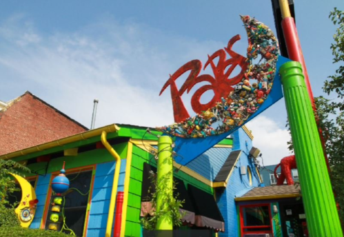 Colorful building exterior with a whimsical sign reading "Pats," adorned with various objects and bright colors.