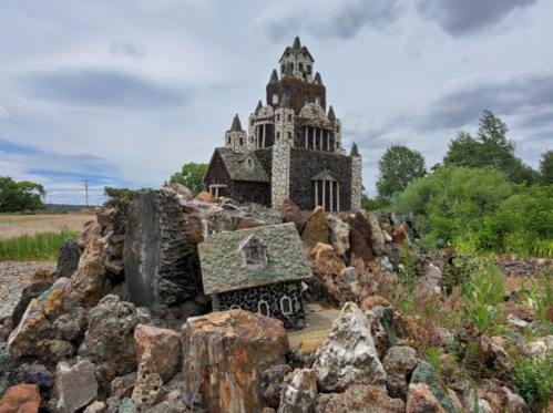 A whimsical stone castle surrounded by colorful rocks and greenery under a cloudy sky.