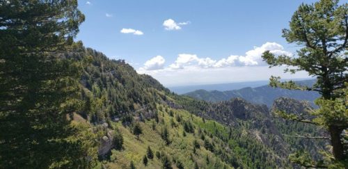 A scenic view of mountains and trees under a blue sky with clouds, showcasing a lush green landscape.
