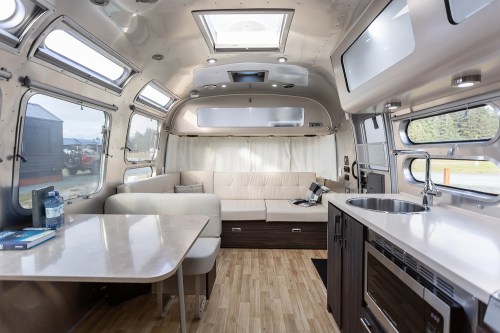 Interior of a modern camper van featuring a cozy seating area, kitchenette, and large windows for natural light.