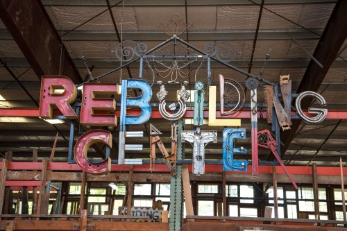 Colorful sign reading "Rebuilding Center" made from various materials, hanging in a warehouse setting.