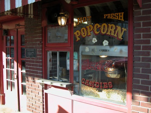 A vintage popcorn stand with a red brick exterior, featuring a sign that reads "Hot Fresh Popcorn" and "Candies."