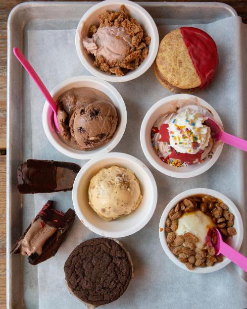 A tray with various ice cream bowls, including chocolate, vanilla, and toppings, alongside cookies and cake slices.