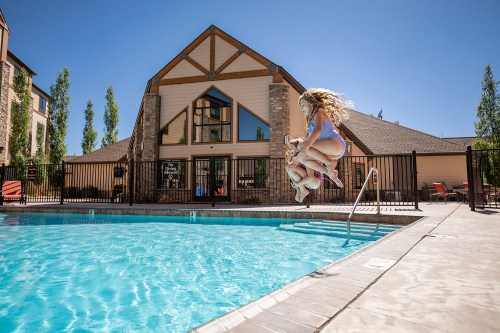 A child jumps into a swimming pool in front of a large building on a sunny day.