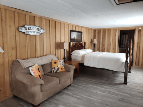 Cozy room with wooden walls, a sofa, and two beds, featuring a "Welcome to the Farm" sign.