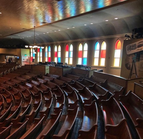 Interior of a theater with wooden seating and colorful stained glass windows, creating a vibrant atmosphere.