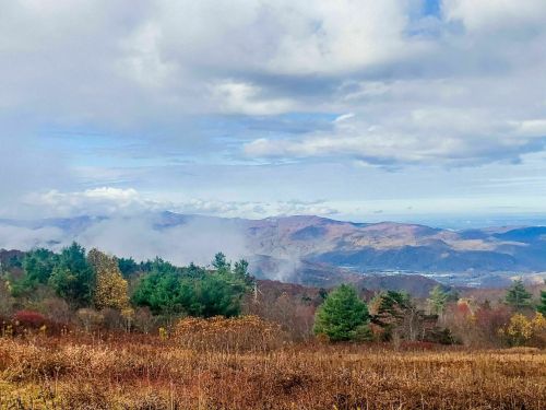 A scenic view of mountains with mist, trees, and a cloudy sky, showcasing autumn colors in the landscape.