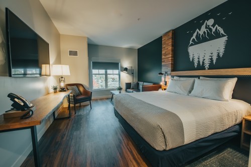 Cozy hotel room with a king bed, wooden accents, a large window, and mountain-themed wall art.
