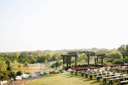 Outdoor wedding venue with wooden benches, a floral arch, and a scenic view of greenery under a clear sky.