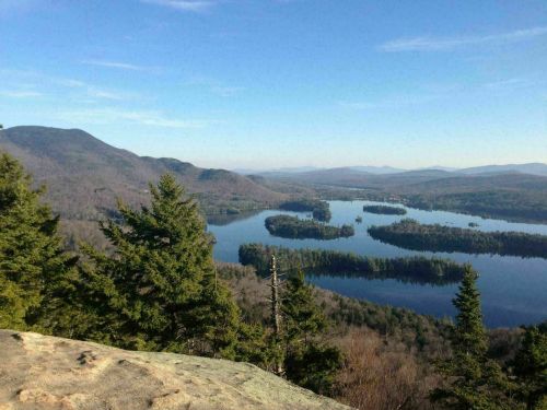 A scenic view of a lake surrounded by mountains and trees under a clear blue sky.