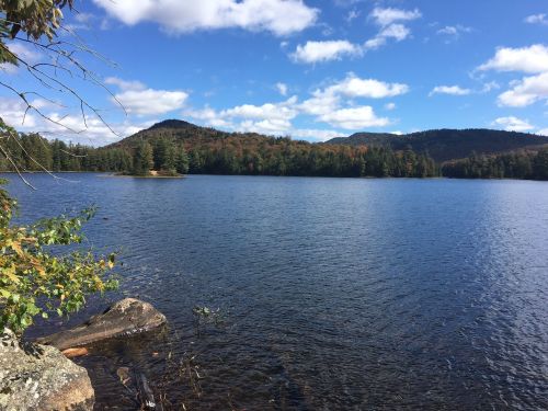 A serene lake surrounded by trees and mountains under a blue sky with fluffy clouds.