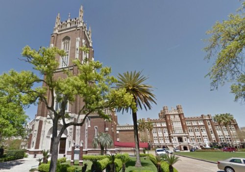 A tall brick tower with a clock stands beside a large building, surrounded by palm trees and green landscaping.