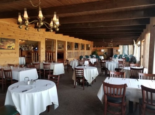 Interior of a restaurant featuring wooden beams, round tables with white tablecloths, and a cozy atmosphere.