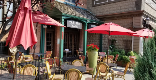 Outdoor seating area of Tartine Wine Bar, featuring red umbrellas and bistro tables in a charming setting.