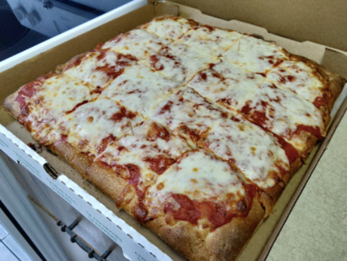 A square pizza with melted cheese and tomato sauce, cut into 16 slices, in a cardboard box.