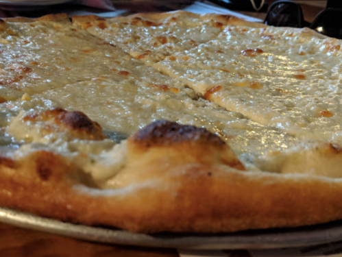 A close-up of a cheese pizza with a golden crust, sliced into pieces, on a metal tray.