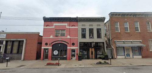 A street view of two historic buildings, one pink and one gray, with storefronts and decorative details.