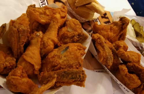 A platter of crispy fried chicken pieces served with pickles and bread on the side.