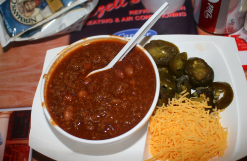 A bowl of chili with beans, served with sliced jalapeños and shredded cheese on a white plate.