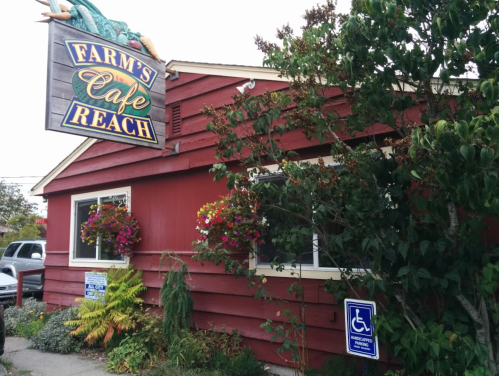 A red wooden building with a sign reading "Farm's Cafe Reach" and flower baskets by the windows.