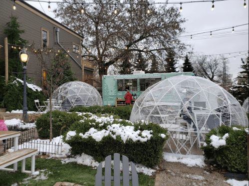 Outdoor dining area with clear igloo-like structures, snow on the ground, and a food truck in the background.