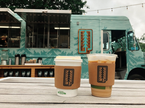 A coffee truck with a teal exterior, featuring two coffee cups on a wooden table in the foreground.