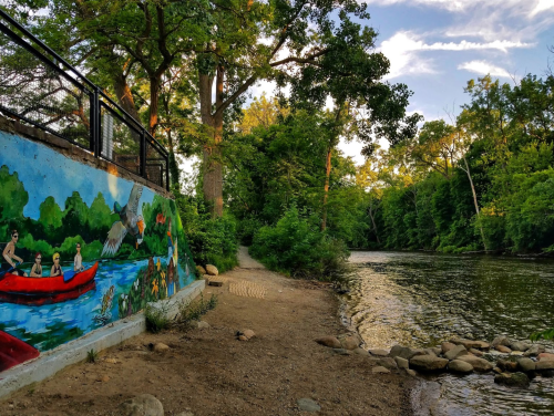 A vibrant mural of people kayaking beside a serene river, surrounded by lush greenery and a clear blue sky.