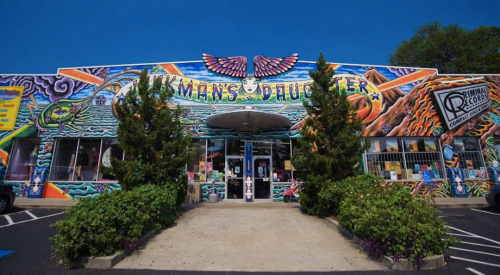 Colorful mural on the exterior of a shop named "Hickman's Daughter," surrounded by greenery and a clear blue sky.