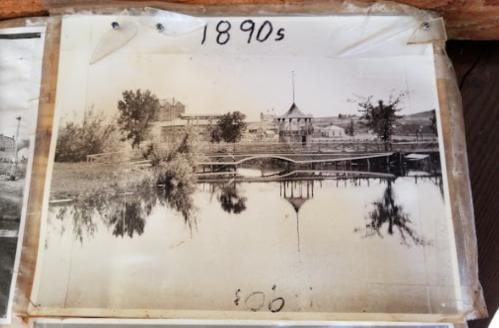 Black and white photo from the 1890s showing a bridge and a building reflected in a calm body of water.
