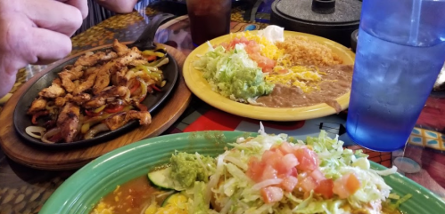 A colorful spread of Mexican dishes, including sizzling fajitas, rice, beans, and a salad topped with guacamole and tomatoes.