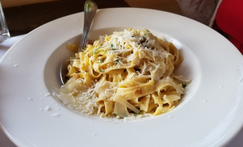 A plate of fettuccine pasta topped with grated cheese and herbs, served with a spoon on the side.