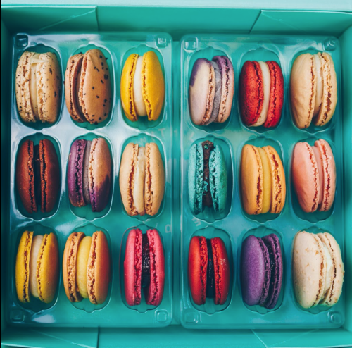 A colorful assortment of macarons in a teal box, featuring various flavors and vibrant colors.