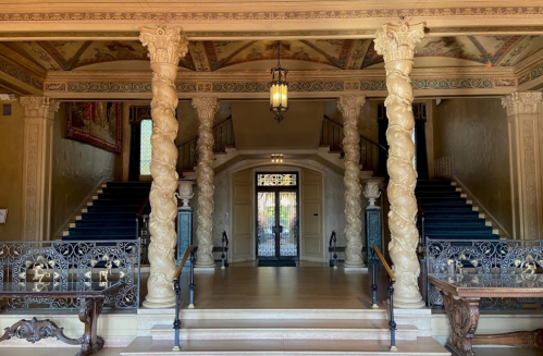 Grand entrance hall with ornate columns, a chandelier, and a staircase leading to an upper level. Elegant decor throughout.