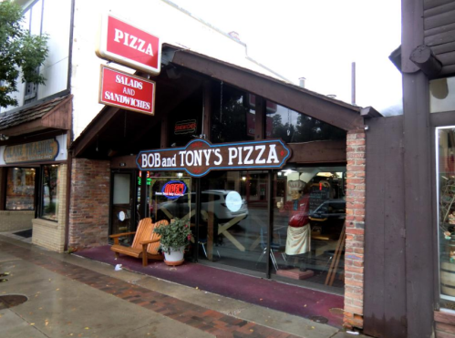 Exterior of Bob and Tony's Pizza, featuring a sign and open door, with outdoor seating and nearby shops.