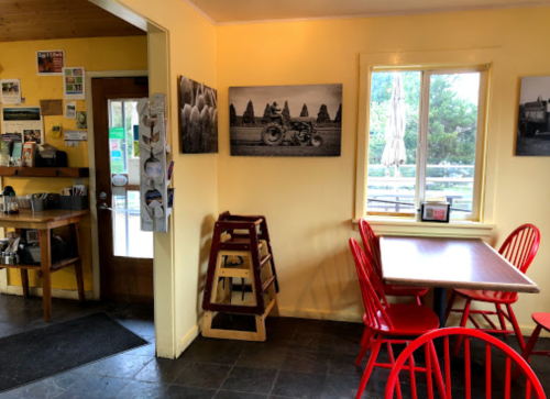 Cozy café interior with yellow walls, red chairs, a wooden table, and black-and-white photos on display.
