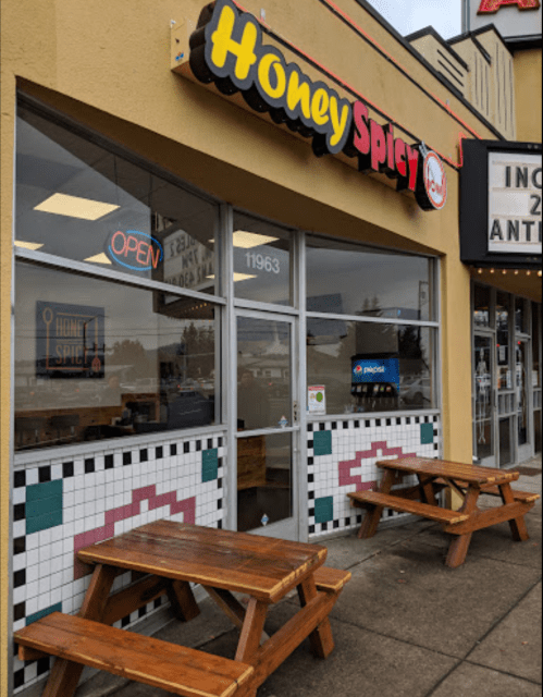 Exterior of Honey Spicy restaurant with an open sign, featuring wooden tables and colorful tile accents.