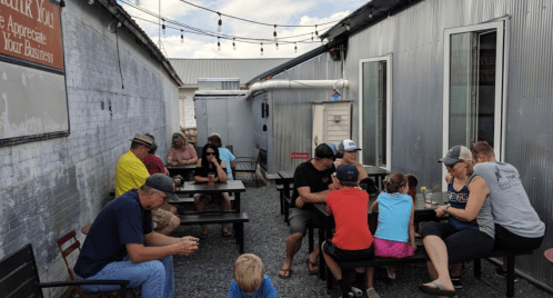 A lively outdoor seating area with people dining and socializing at tables between two buildings.
