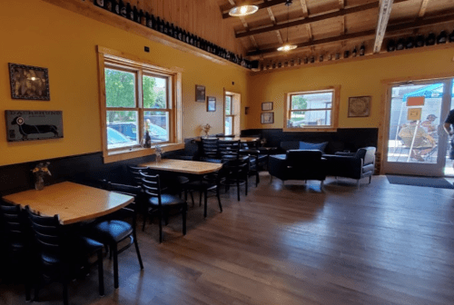 Cozy interior of a restaurant with wooden tables, black chairs, and yellow walls, featuring large windows and a welcoming entrance.