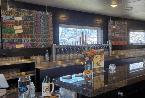 A bar with a chalkboard menu displaying drink options and prices, and a row of beer taps in the background.