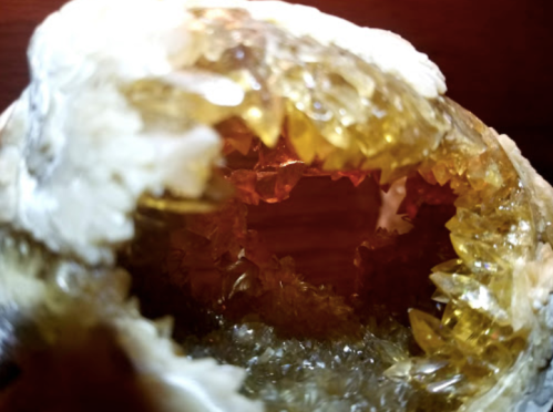 Close-up of a geode with golden crystals and a rough, white exterior, revealing a sparkling interior.