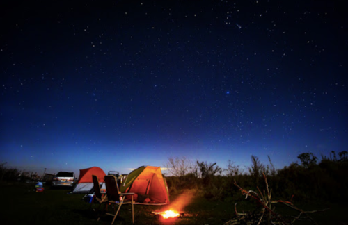 A campsite at night with tents, a campfire, and a starry sky above.