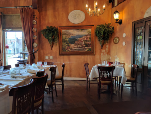 Cozy restaurant interior with wooden tables, chairs, and a large painting on the wall, featuring warm, earthy tones.