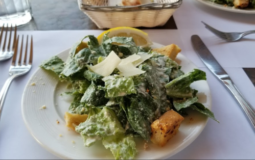 A plate of Caesar salad with romaine lettuce, croutons, Parmesan cheese, and a lemon wedge.