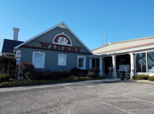 A winery building with a sign reading "WINERY," surrounded by landscaping and a clear blue sky.