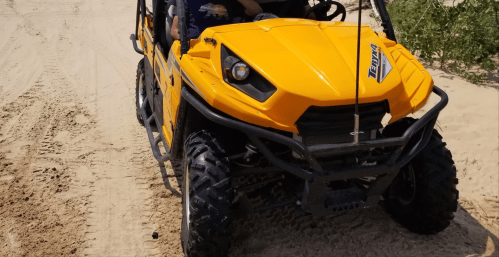A bright yellow off-road vehicle parked on sandy terrain, with two people seated inside.