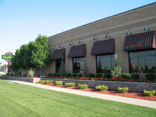 Exterior view of a restaurant with striped awnings, landscaped greenery, and a sign reading "Mallie's."