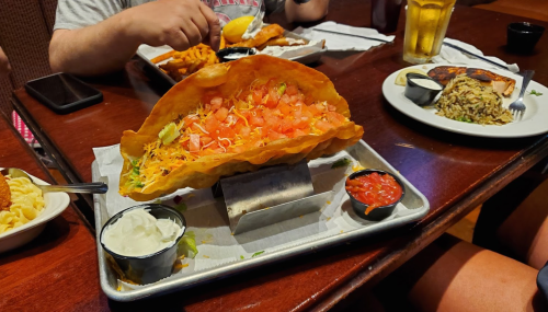 A large taco salad in a crispy shell, topped with tomatoes and lettuce, served with salsa and sour cream on the side.
