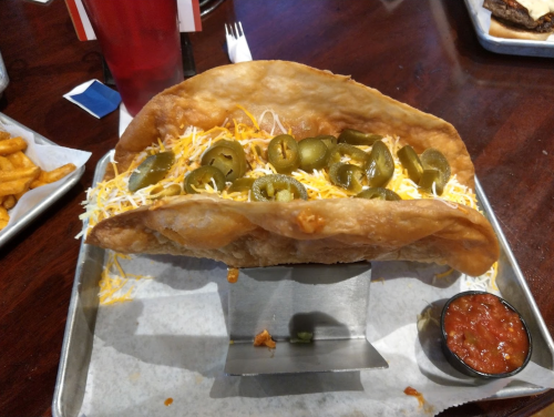 A large taco shell filled with cheese and jalapeños, served with a side of salsa on a metal tray.