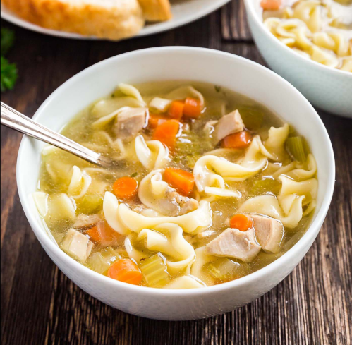A bowl of chicken noodle soup with carrots, celery, and pasta, served on a wooden table.