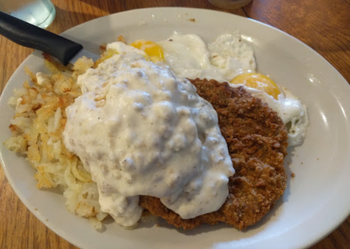 A plate of chicken fried steak topped with creamy gravy, served with hash browns and two fried eggs.